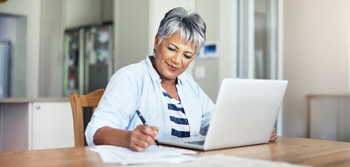 A woman is using a laptop and taking notes at a table during an Unjury Cares Support Group Meeting.