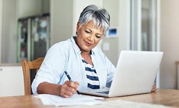 Woman using a laptop and taking notes at a table during an Unjury Support Group meeting.